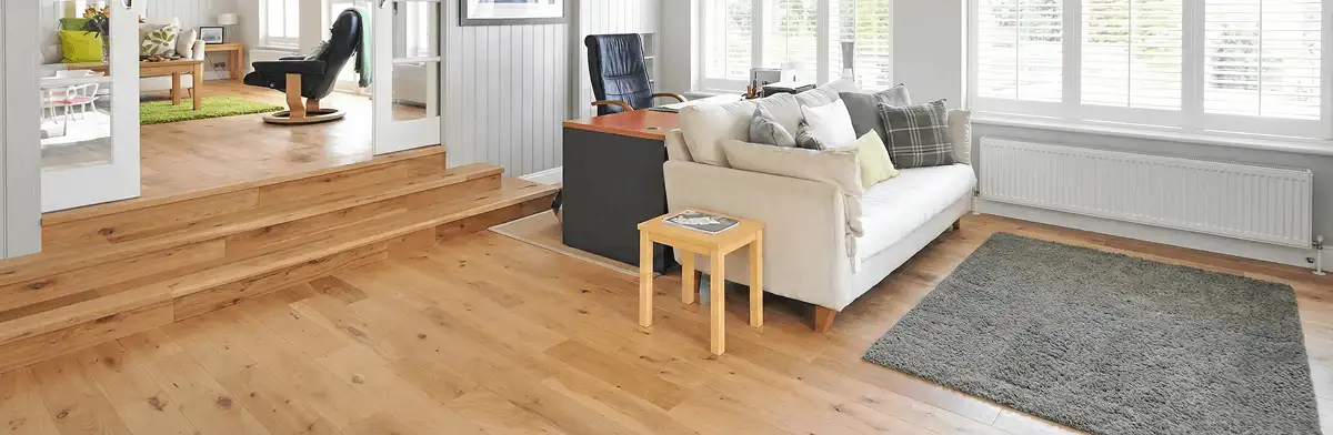 A modern living room with professionally installed laminate flooring, a beige sofa, a small side table, a gray rug, and large windows with white shutters in San Jose, CA